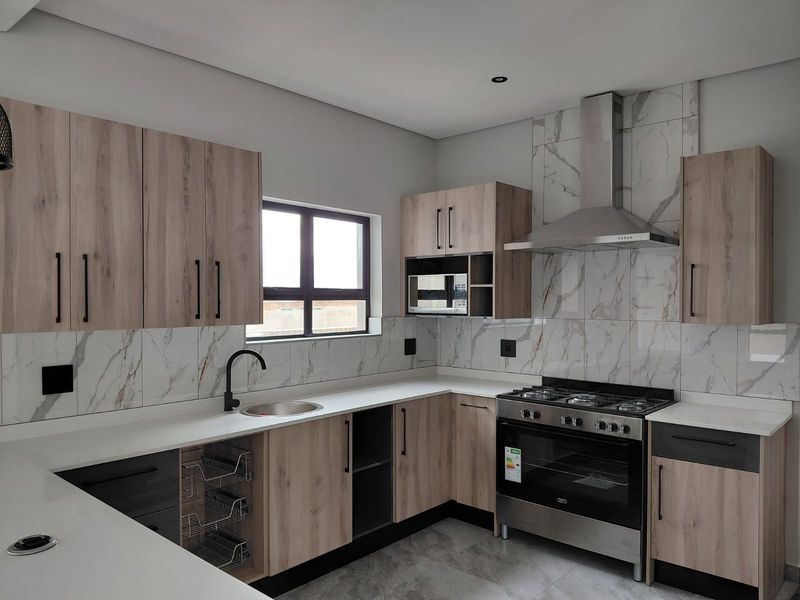 Modern kitchen featuring light wood-grain cabinetry, marble-effect tiled backsplash, stone countertops, and a stainless steel gas stove with extractor fan.
