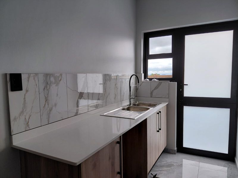 A modern scullery area featuring marble-look splashback tiles, stone-effect countertops, a stainless steel double sink, and a glass-paneled exterior door.
