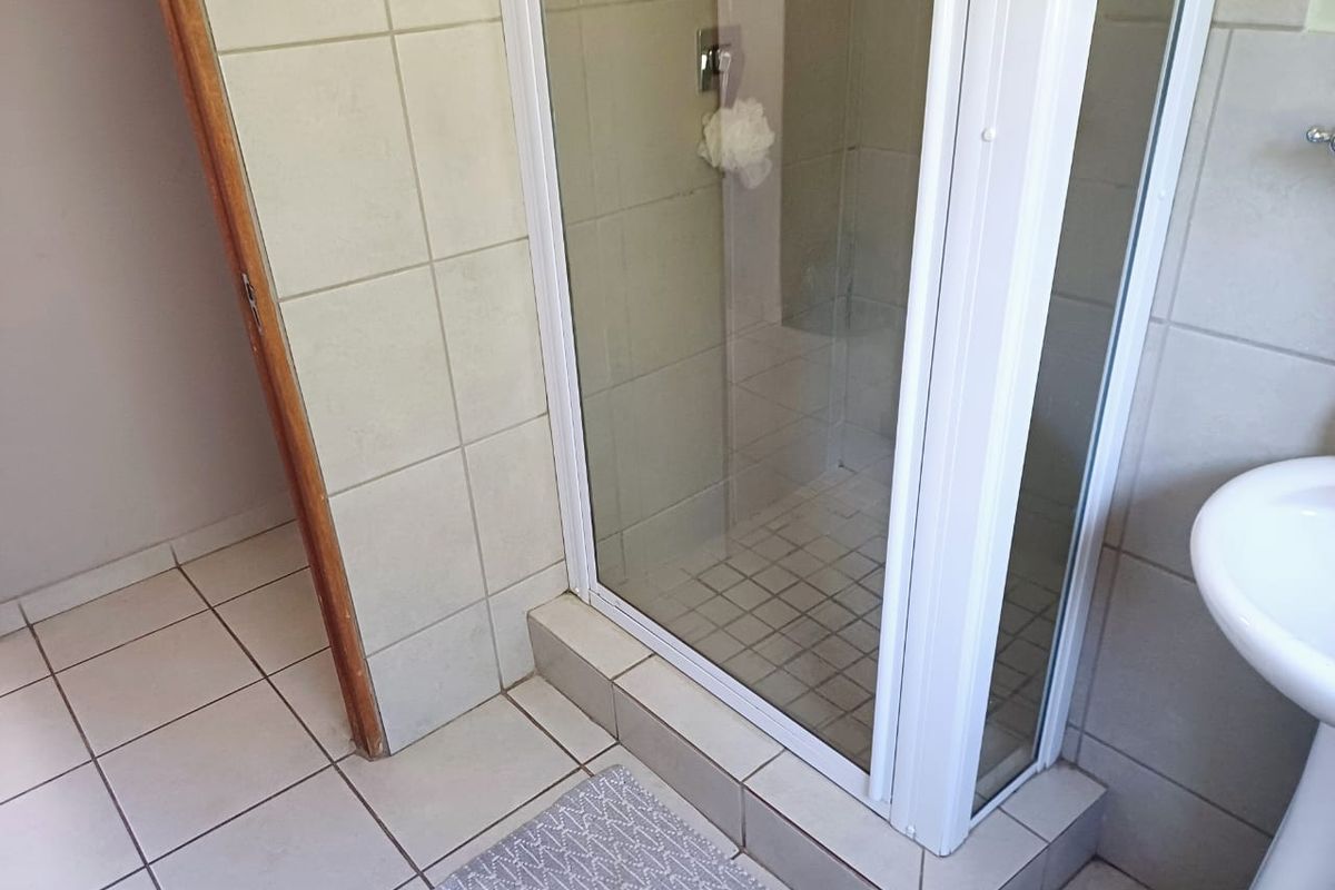 A functional bathroom featuring a corner shower enclosure with glass doors and a pedestal basin, finished with neutral wall and floor tiling.