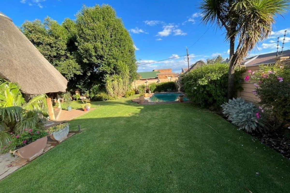 A well-maintained rear garden featuring a lush green lawn, a swimming pool, and a thatched-roof patio area.