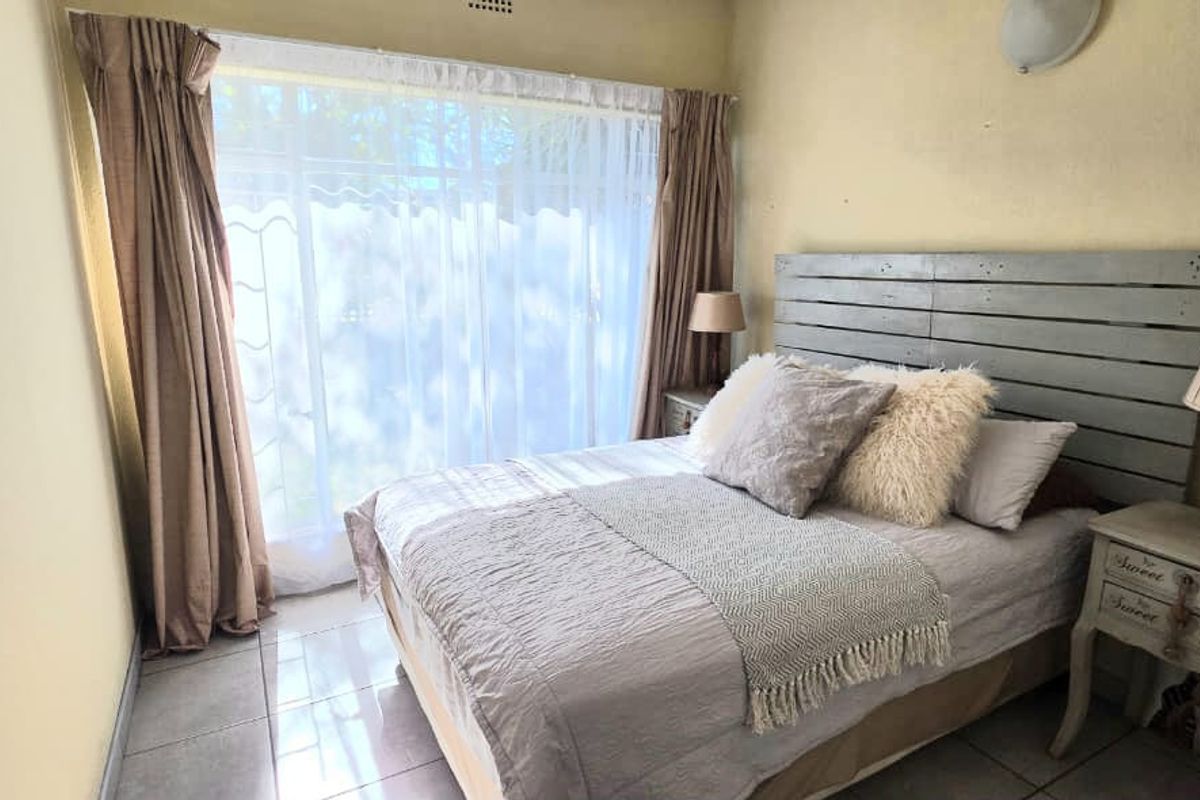 A compact bedroom featuring tiled flooring, a large window with curtains, and a wall-mounted light fixture.