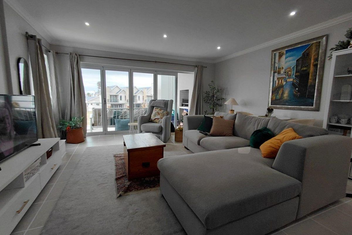 A bright and spacious living room featuring tiled flooring, recessed downlighting, and large sliding glass doors that provide access to an outdoor balcony area.