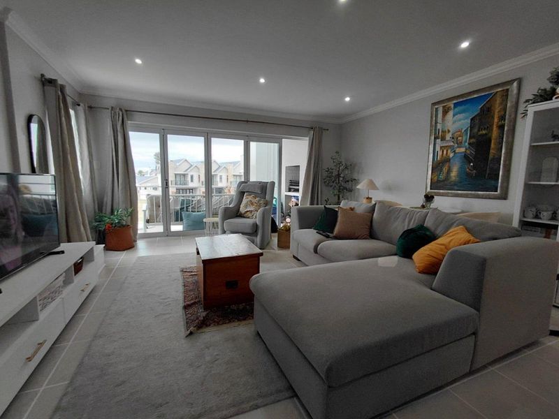 A bright and spacious living room featuring tiled flooring, recessed downlighting, and large sliding glass doors that provide access to an outdoor balcony area.