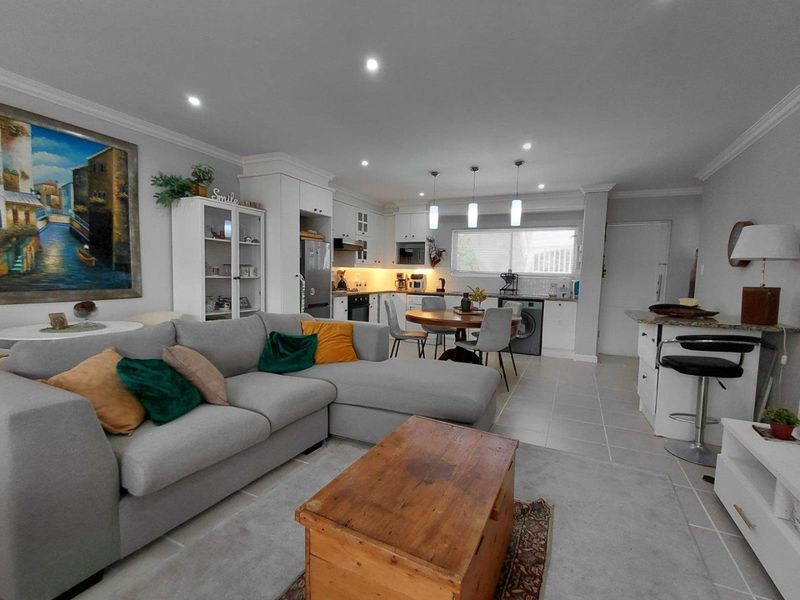 Spacious open-plan living area featuring a modern kitchen with built-in cabinetry, island breakfast bar, and integrated laundry facilities, finished with neutral floor tiles.