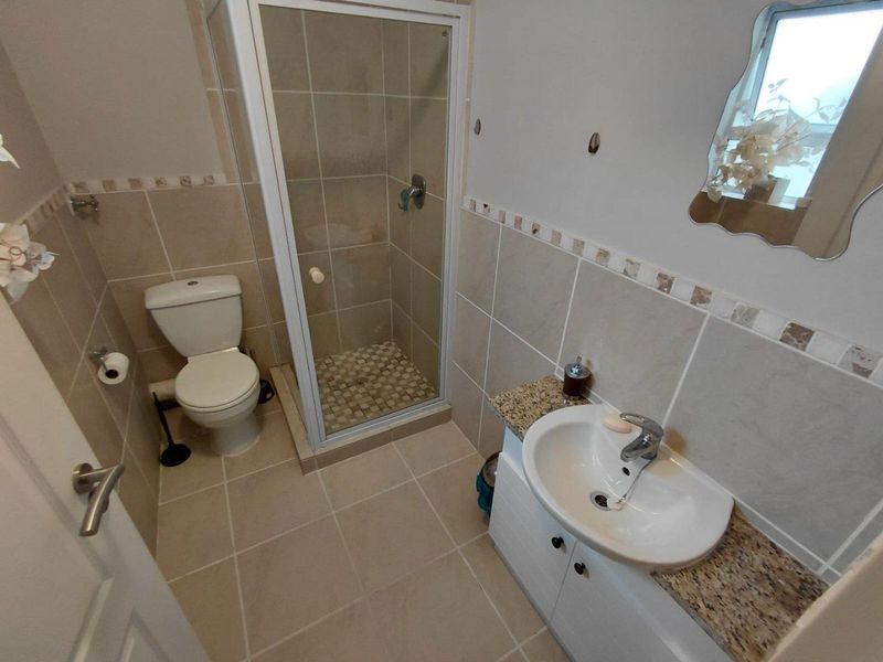 A functional bathroom featuring a shower enclosure, a vanity cabinet with a granite countertop, and neutral ceramic tiling throughout.