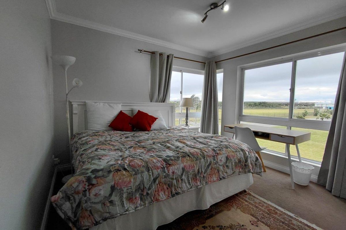 A bedroom featuring large sliding windows with natural light, neutral wall finishes, and a ceiling-mounted spotlight fixture.