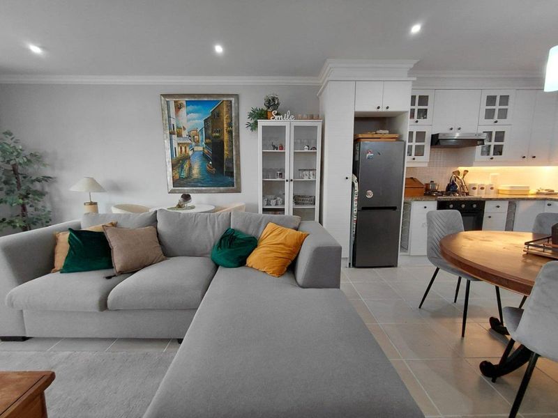 An open-plan living and kitchen area featuring modern white cabinetry, integrated appliances, tiled flooring, and recessed lighting, creating a bright and functional living space.