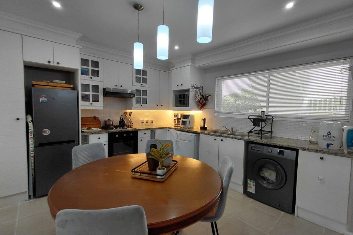 A well-maintained kitchen featuring white cabinetry, granite countertops, tiled backsplash, integrated appliances, and modern pendant lighting.