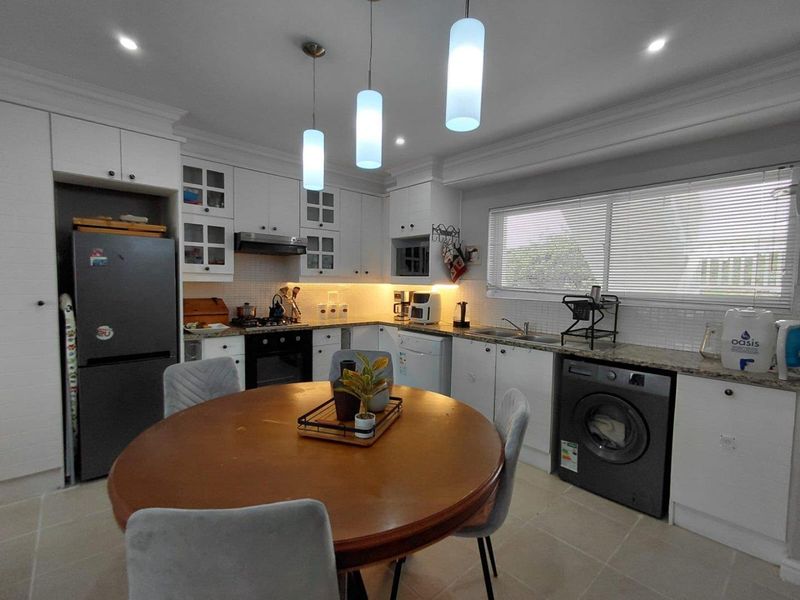 A well-maintained kitchen featuring white cabinetry, granite countertops, tiled backsplash, integrated appliances, and modern pendant lighting.