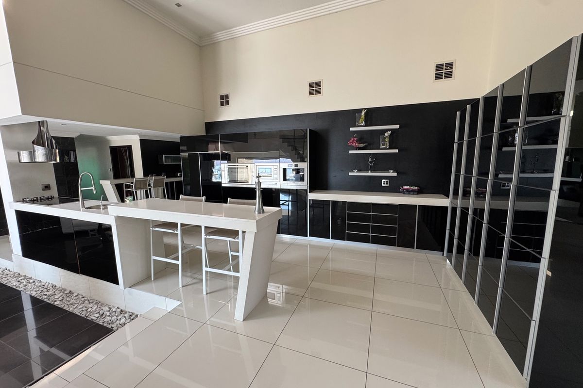 Modern kitchen featuring high-gloss black cabinetry, white stone countertops, a central island with breakfast bar, and integrated built-in appliances.