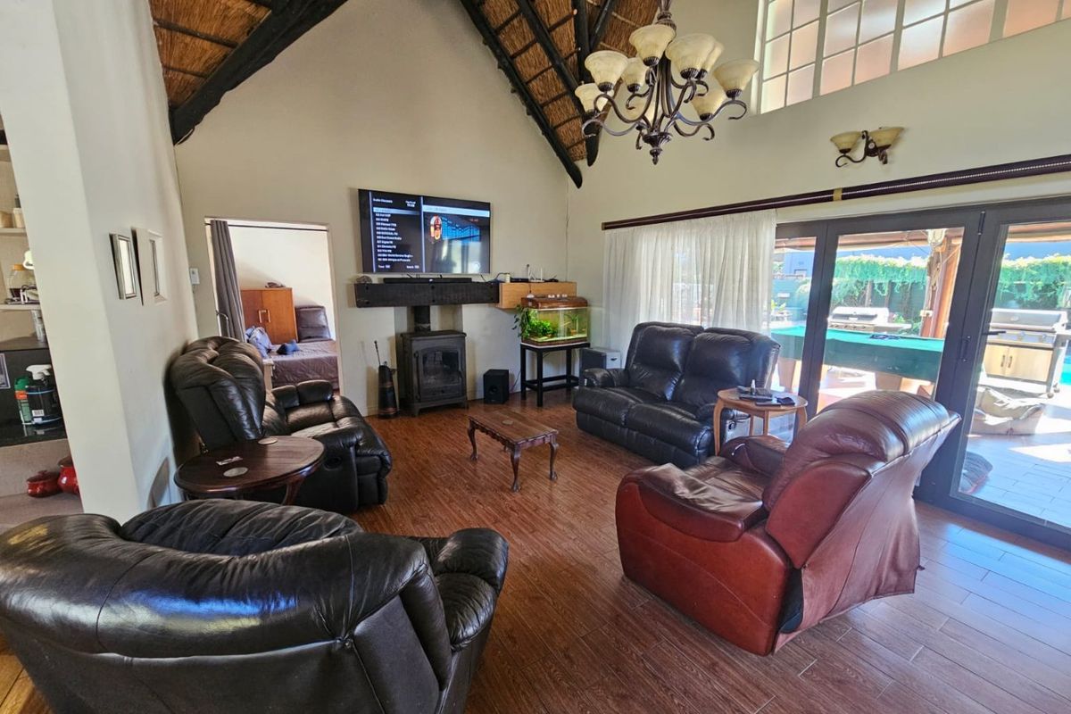 Spacious living room featuring a high vaulted thatched ceiling, wood-burning fireplace, and large sliding glass doors opening to an outdoor patio area.