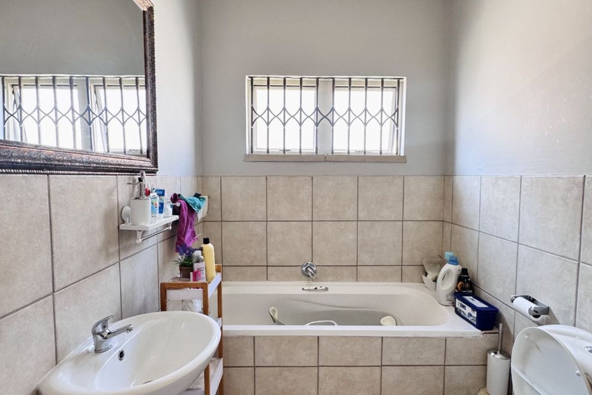 A functional bathroom featuring a pedestal basin, a built-in bathtub with tiled surround, and a toilet, finished with neutral wall and floor tiles.