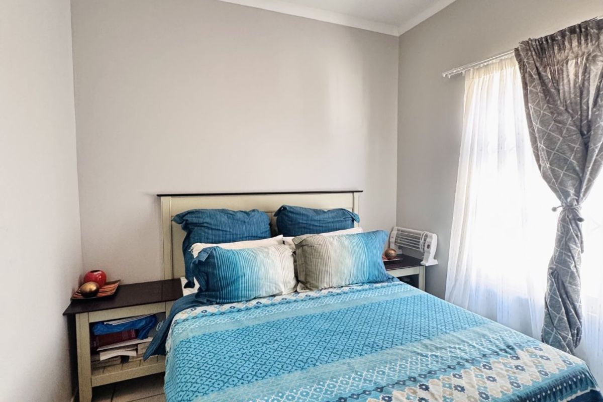 A compact bedroom featuring tiled flooring, neutral wall finishes, and a window with curtain treatments.