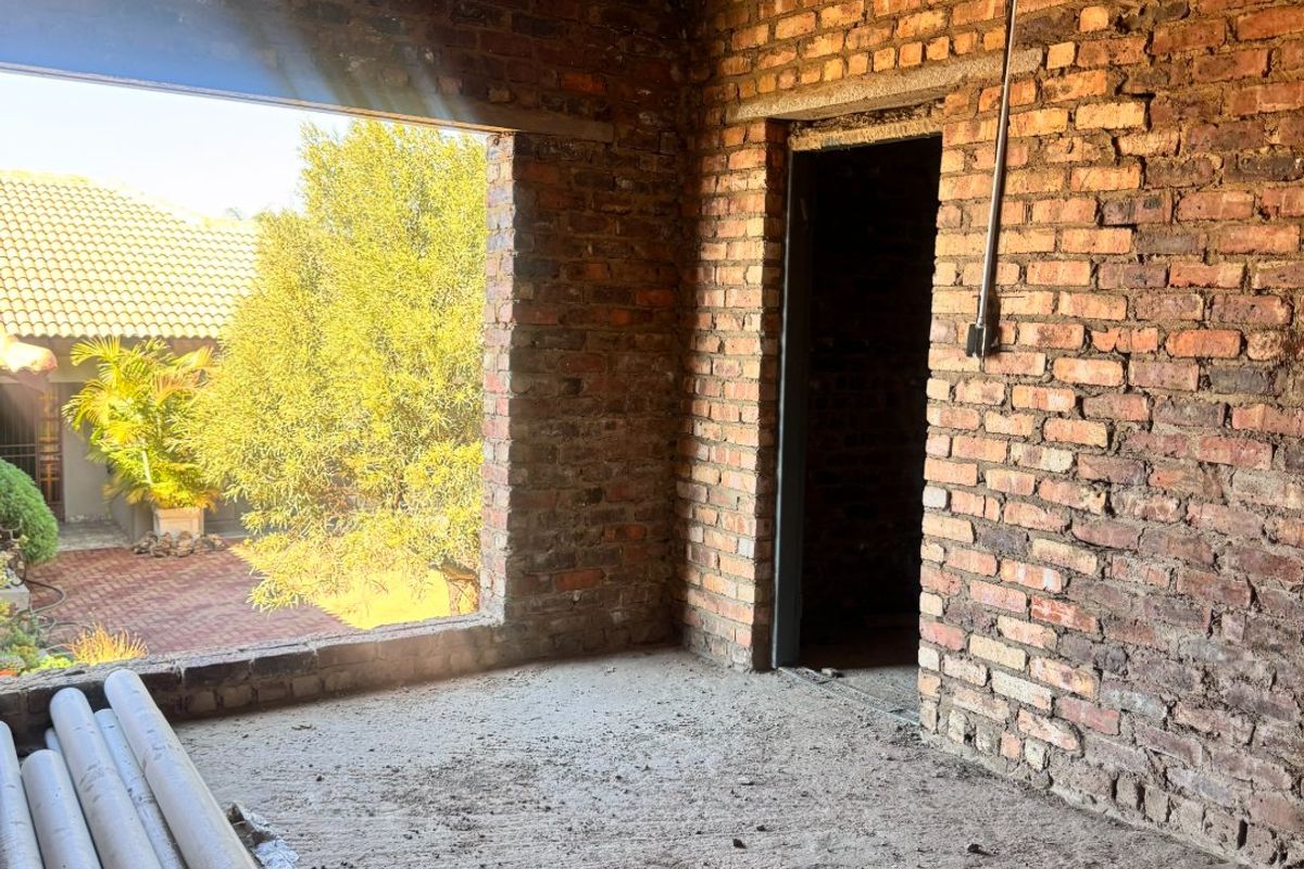 An unfinished interior room in shell condition featuring exposed brick walls, a concrete ceiling, and an open doorway leading to an outdoor area.