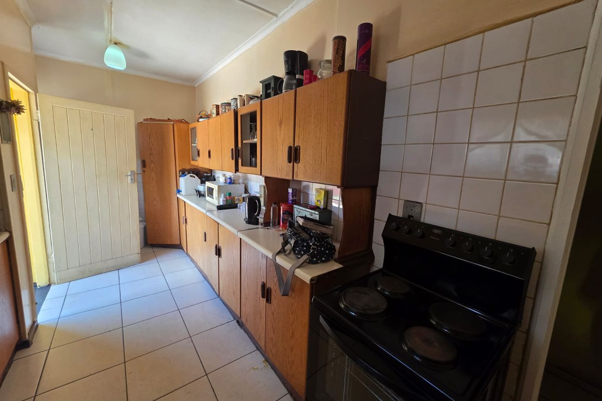 A functional kitchen featuring dated laminate cabinetry, tiled flooring, and a tiled splashback with a freestanding electric stove.