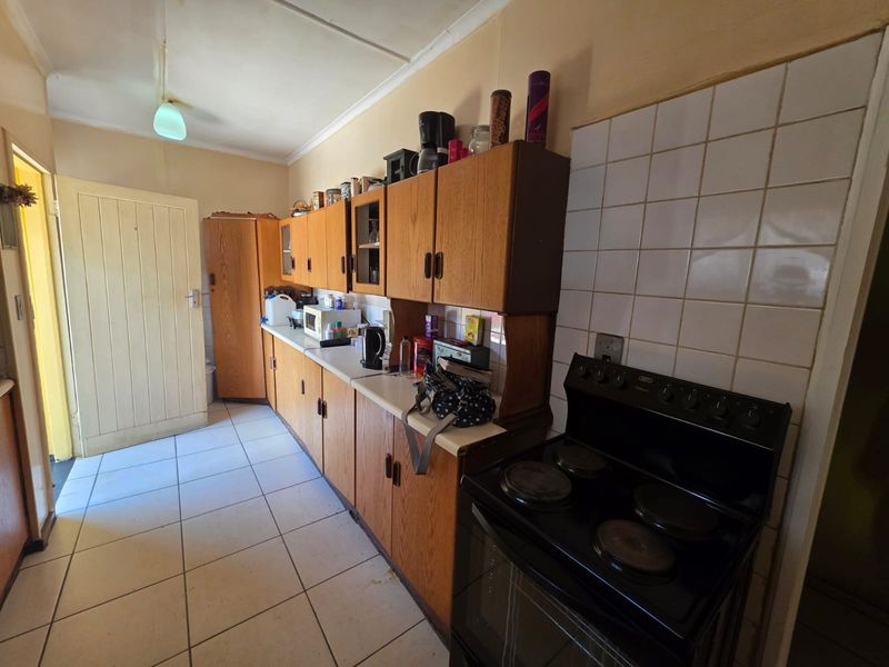 A functional kitchen featuring dated laminate cabinetry, tiled flooring, and a tiled splashback with a freestanding electric stove.