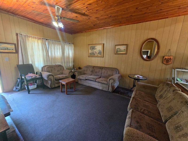 A living room featuring wood-panelled walls and a timber-clad ceiling, offering a dated aesthetic with potential for modernization.