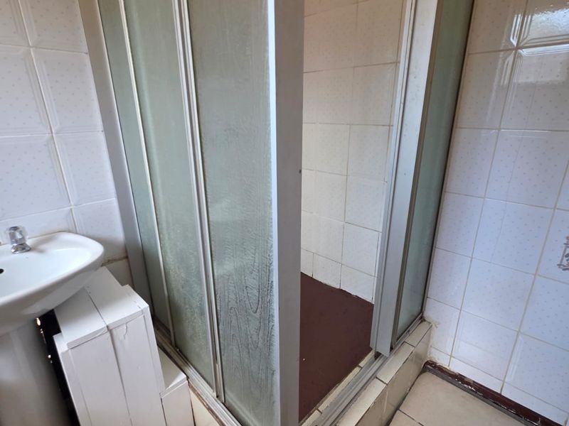 A dated bathroom featuring a pedestal sink and a shower enclosure with tiled walls and flooring, requiring modernization and cosmetic updates.