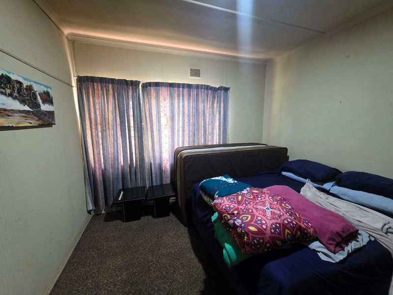 A bedroom featuring carpeted flooring and a ventilation grille, requiring cosmetic updates to improve the overall aesthetic and condition of the space.
