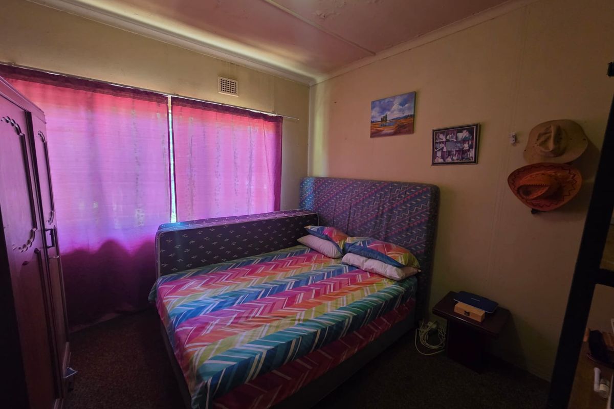 A bedroom featuring a ventilation grille, with visible signs of wear including peeling ceiling paint and aged carpeting.