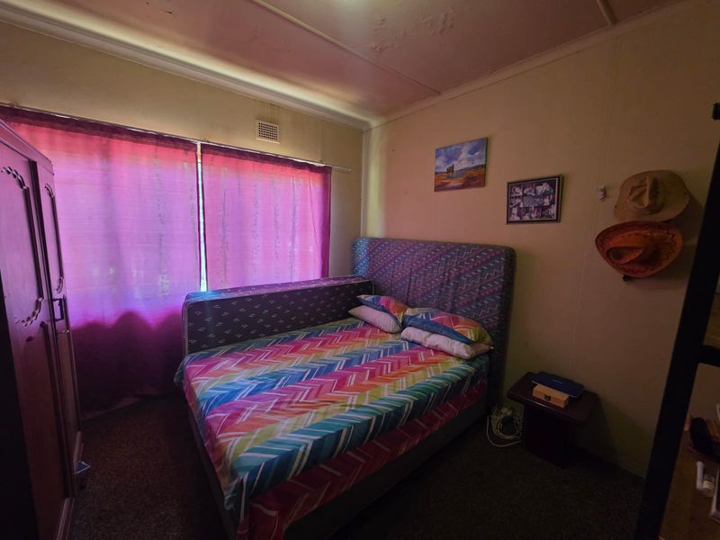 A bedroom featuring a ventilation grille, with visible signs of wear including peeling ceiling paint and aged carpeting.