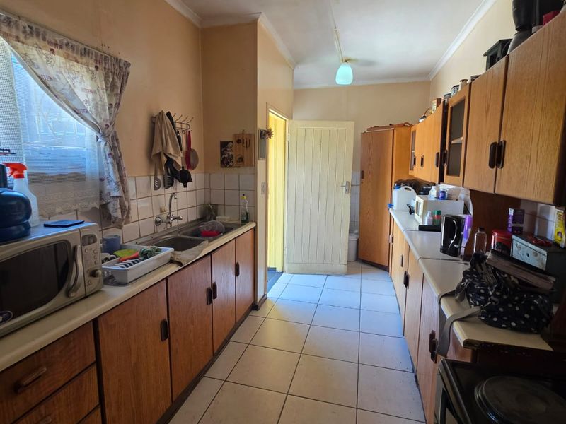 A functional galley-style kitchen featuring wood-look cabinetry, tiled flooring, and a double basin sink, offering potential for a modern renovation.