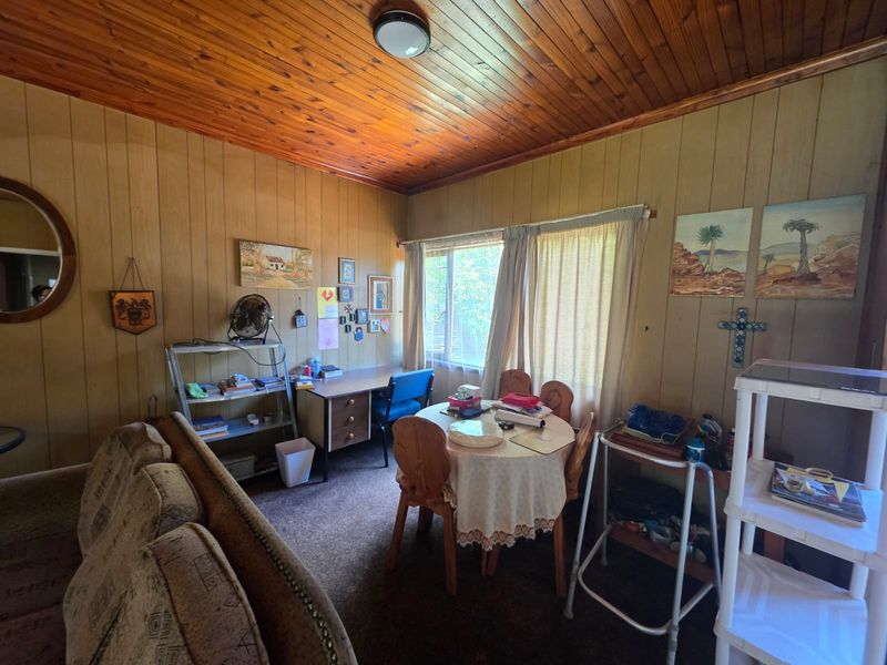 A living area featuring wood-paneled walls and a timber ceiling, offering a dated aesthetic with potential for modernization.