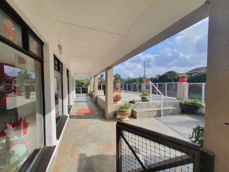 A spacious covered patio area featuring tiled flooring, a glass balustrade, and direct access to an open outdoor terrace.