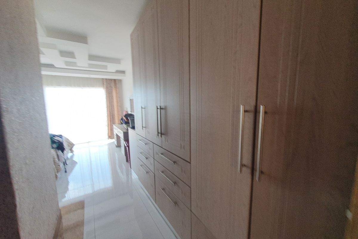 Bedroom featuring extensive built-in wooden cabinetry, modern recessed ceiling design, and polished tiled flooring with natural light access.