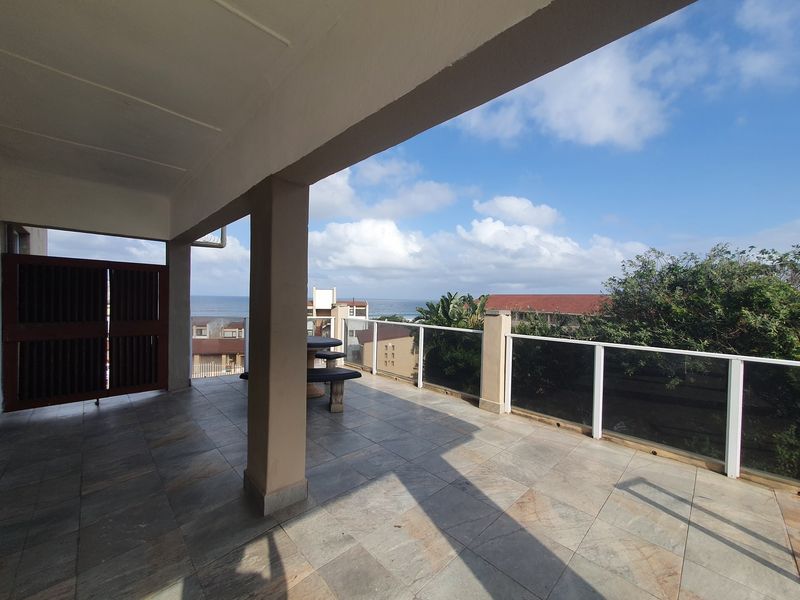 Spacious covered balcony featuring tiled flooring, glass balustrades, and expansive ocean views, providing an ideal outdoor entertainment area.