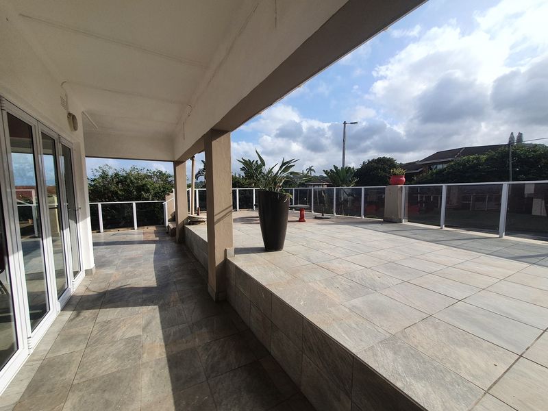 Spacious covered patio featuring tiled flooring and a modern glass balustrade, offering an open outdoor area suitable for commercial or residential use.
