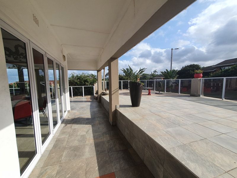 Spacious covered patio featuring tiled flooring and a modern glass balustrade, offering an open outdoor entertainment area with direct access to the interior.