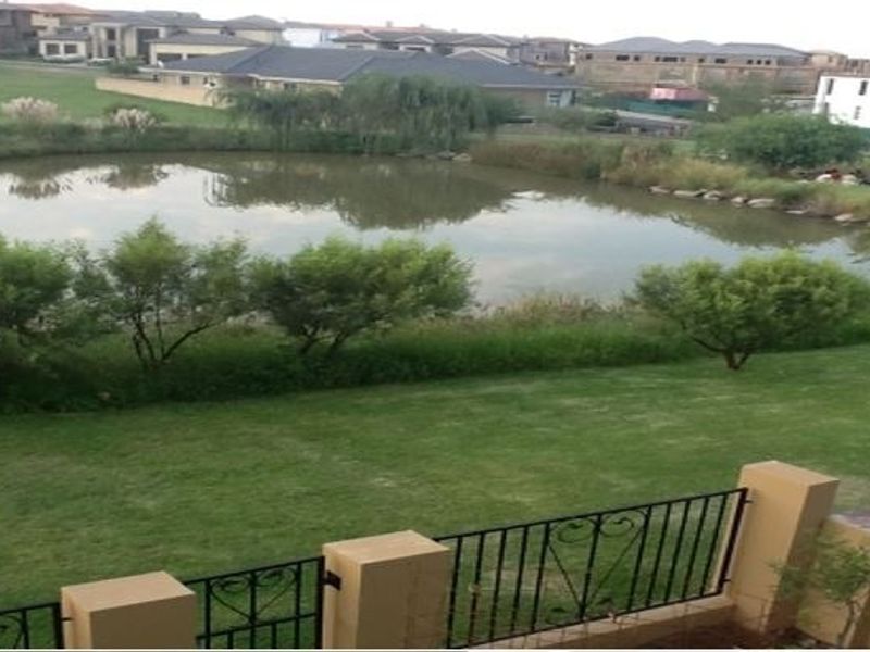A scenic view overlooking a tranquil pond and landscaped garden area, framed by a decorative wrought iron and masonry fence.