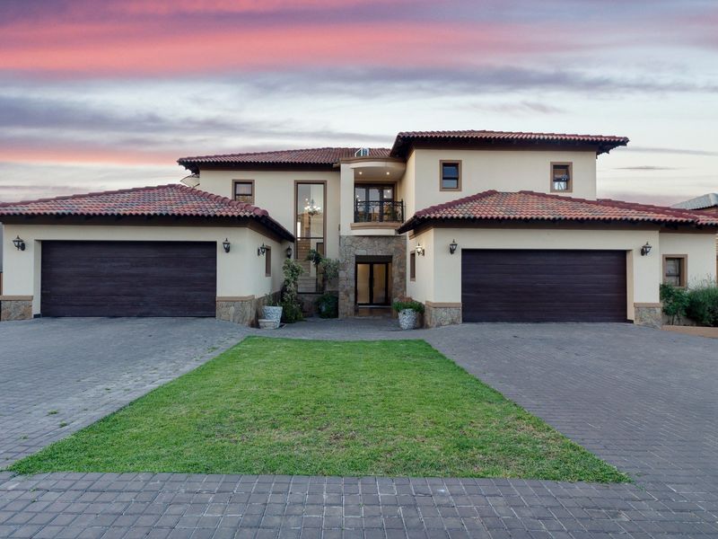 Impressive double-story residence featuring a double garage, stone-clad accents, tiled roof, and a well-maintained paved driveway with a central lawn area.