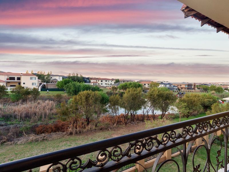 A scenic elevated view overlooking a suburban landscape, pond, and greenery, captured from a balcony with a decorative wrought iron railing.