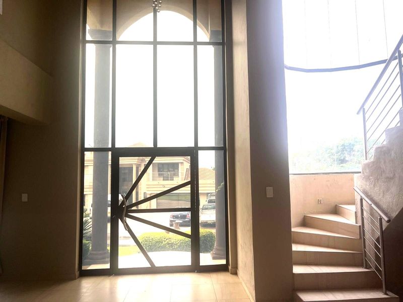 Spacious double-volume entrance hall featuring a large glass door, high ceilings, and a modern staircase with stainless steel balustrades.