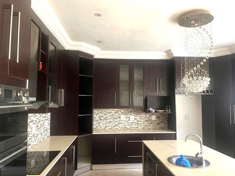 Modern kitchen featuring dark wood cabinetry, stone countertops, a central island with sink, and a decorative crystal chandelier.