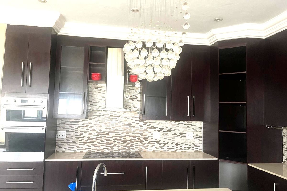 Modern kitchen featuring dark cabinetry, stone countertops, a mosaic tile backsplash, built-in oven, and a prominent decorative chandelier.