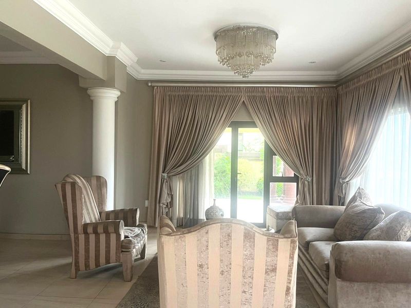 Spacious living room featuring elegant crown molding, a decorative column, tiled flooring, and a glass sliding door providing access to the garden.