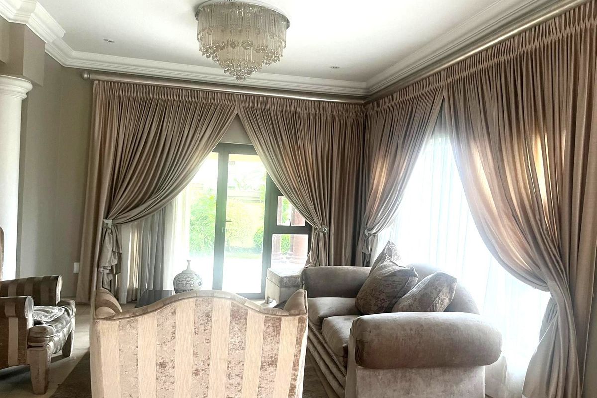 Elegant living room featuring crown molding, a decorative crystal chandelier, and large sliding glass doors with floor-to-ceiling drapery providing access to the exterior.