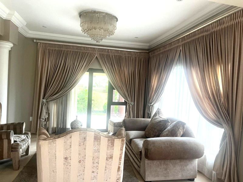 Elegant living room featuring crown molding, a decorative crystal chandelier, and large sliding glass doors with floor-to-ceiling drapery providing access to the exterior.