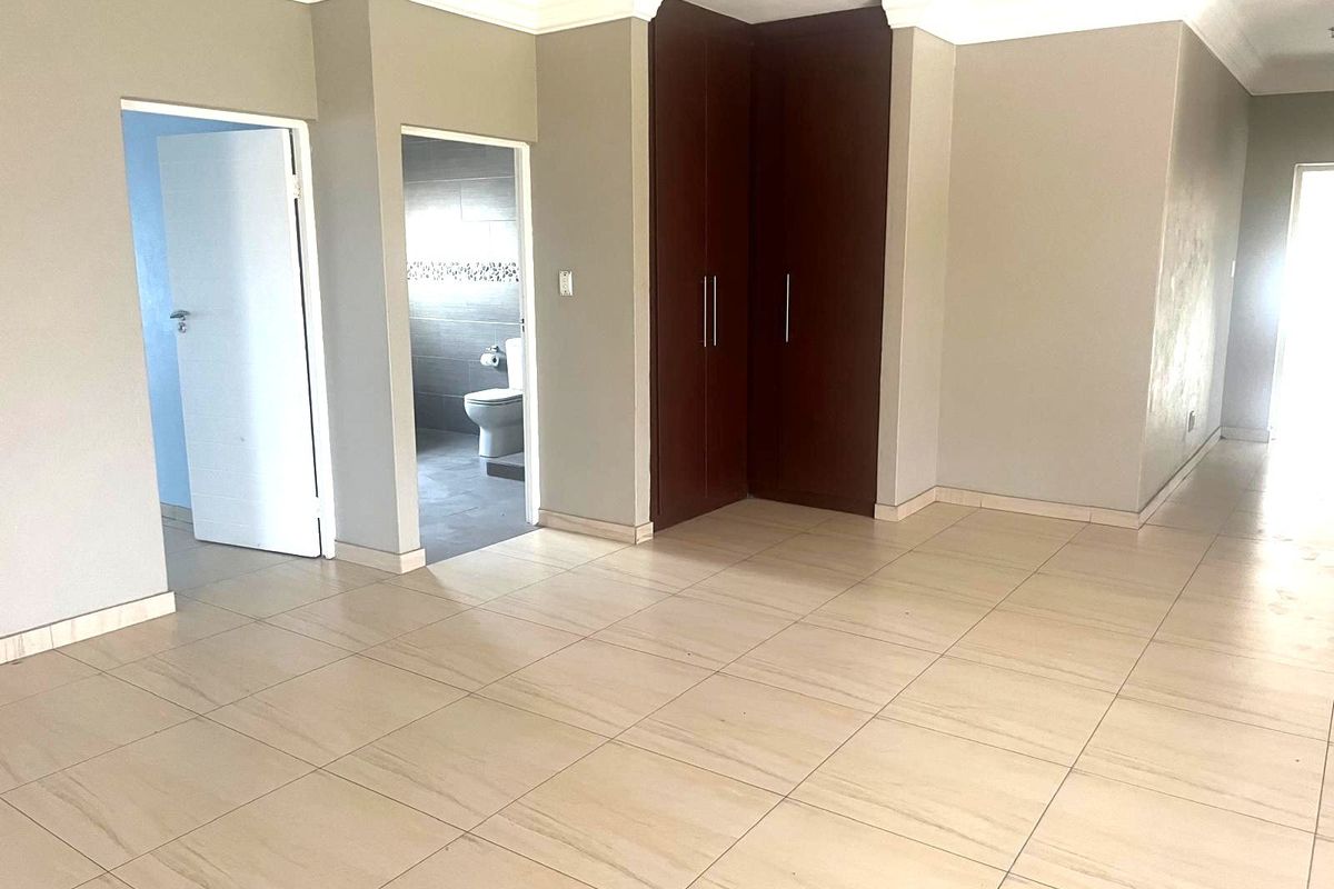 An empty bedroom featuring tiled flooring, built-in cupboards, and access to an en-suite bathroom.