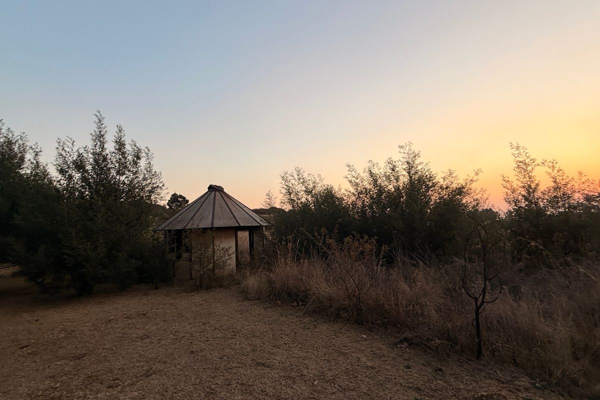 A view of a small detached structure on a vacant residential plot at sunset, surrounded by natural vegetation and open land.