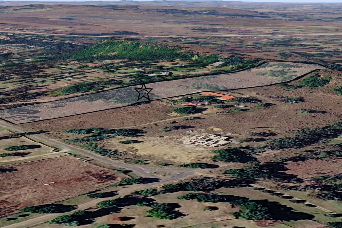 An aerial view of a large vacant residential land plot with clear boundary markings, situated in a rural landscape.