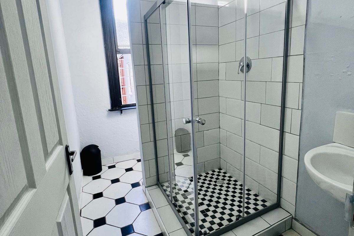 A clean, modern bathroom featuring a glass-enclosed shower, classic black and white tiled flooring, and a pedestal basin.