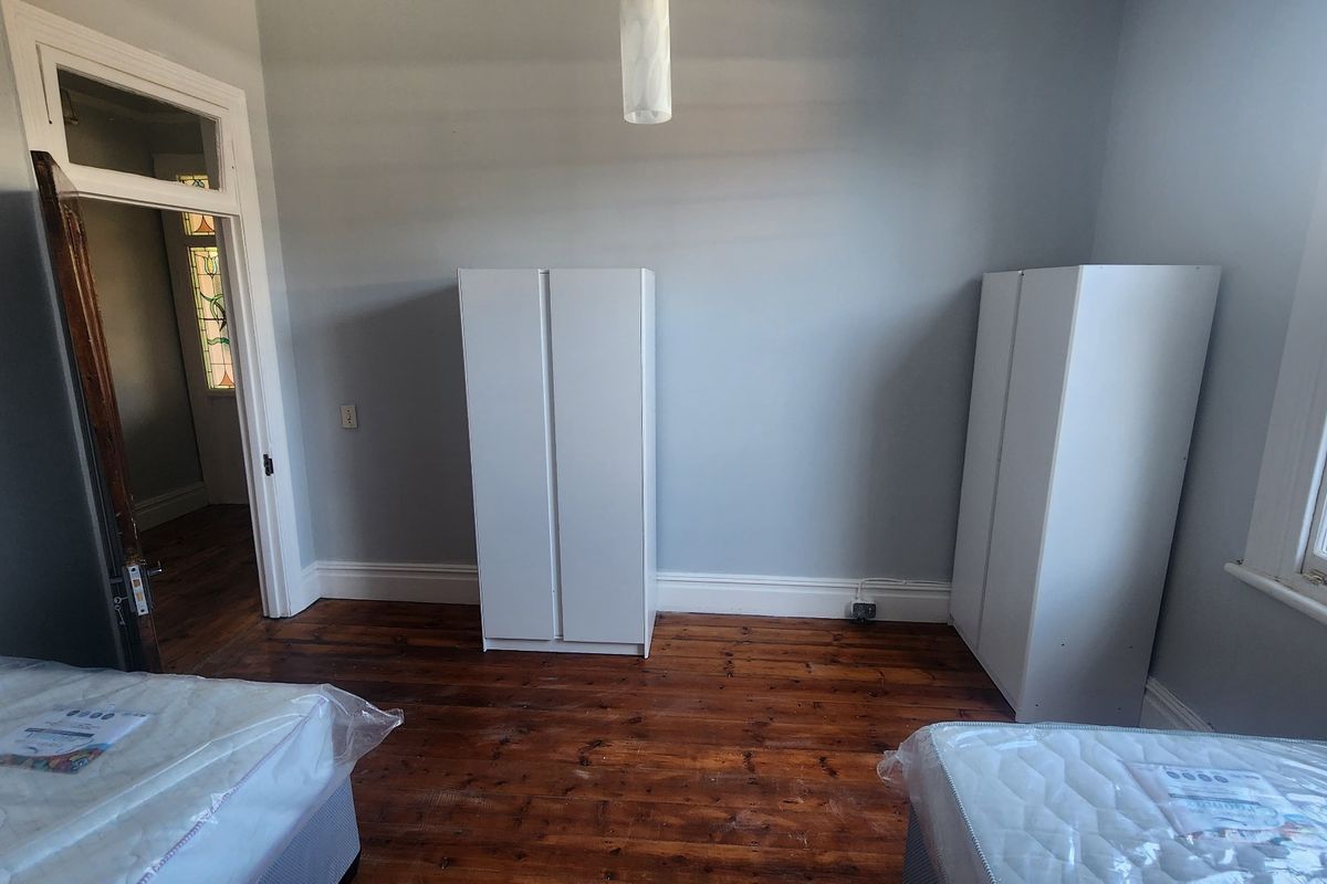 A bedroom featuring original timber flooring, light grey walls, and a characterful stained glass door leading to the hallway.