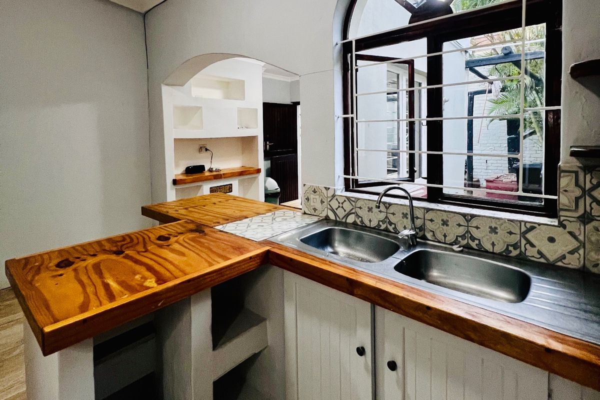 A functional kitchen area featuring a double stainless steel sink, wooden countertops, decorative backsplash tiles, and built-in cabinetry with an arched window.