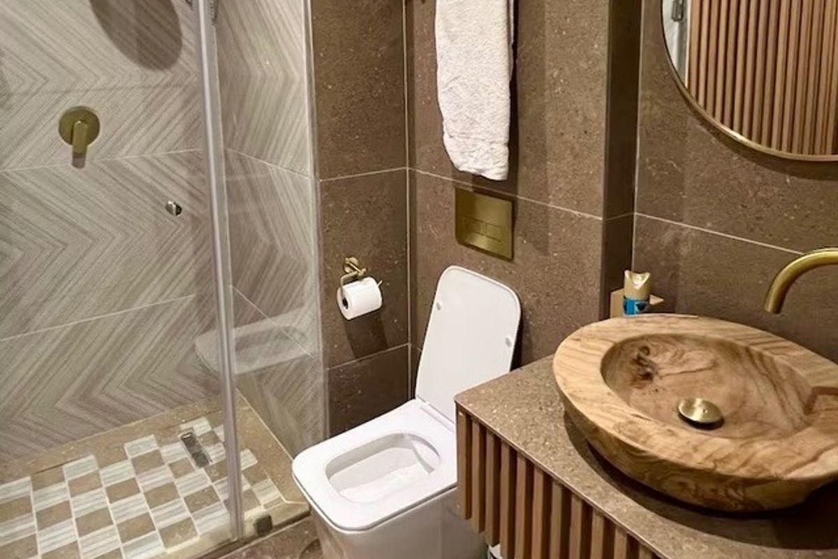 Modern bathroom featuring a walk-in shower with glass screen, wall-mounted toilet, and a unique wooden vessel sink set on a slatted vanity cabinet.