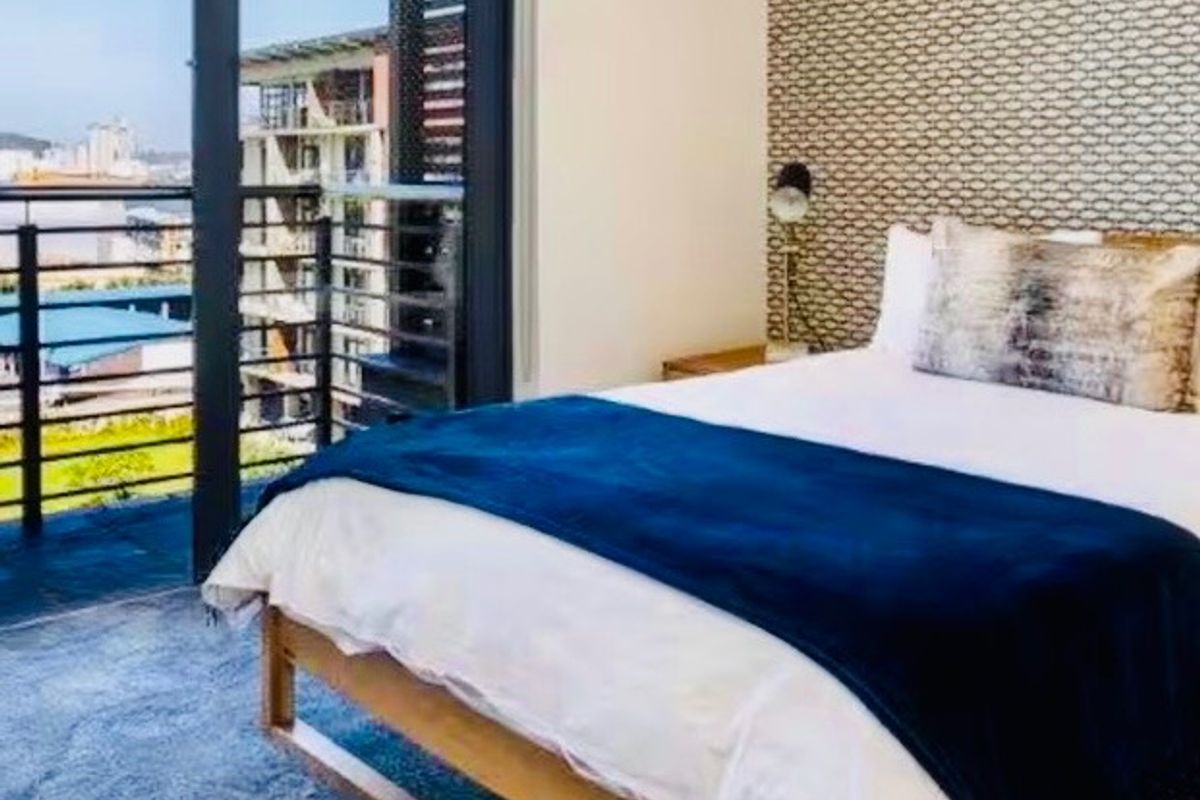 A well-maintained bedroom featuring patterned wallpaper and a sliding glass door that opens onto a private balcony with urban views.