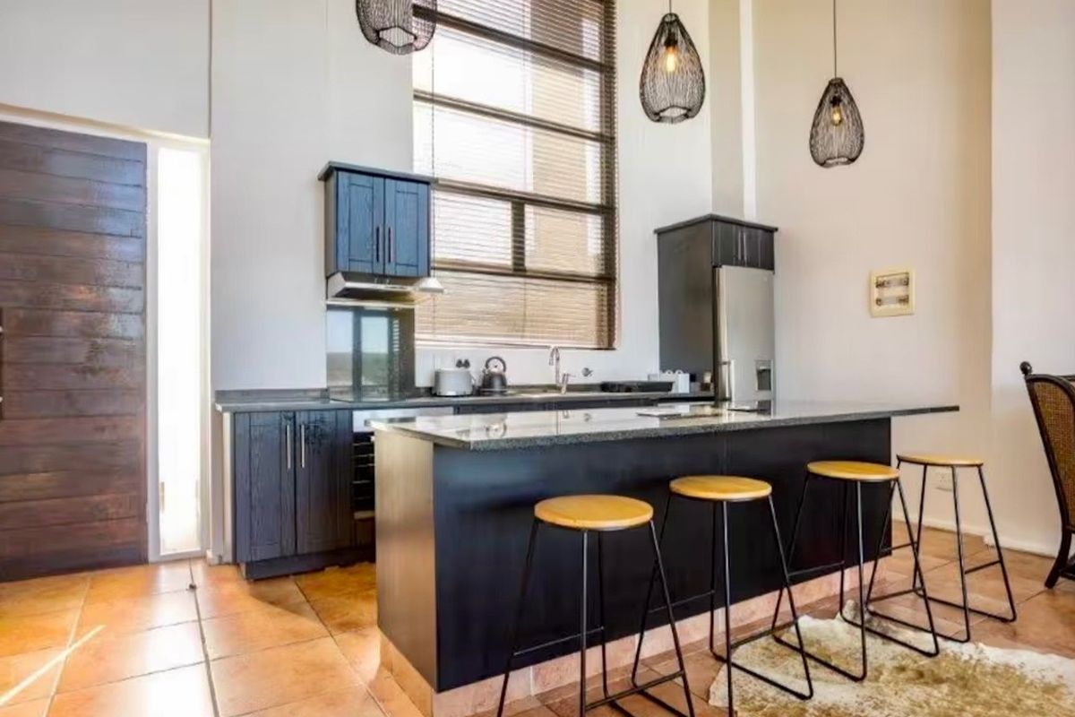 Modern kitchen featuring dark cabinetry, a spacious granite-topped island, tiled flooring, and a large window providing ample natural light.